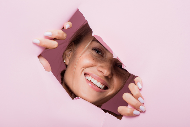 lachende mooie vrouw met sproeten in roze papieren gat - Foto, afbeelding