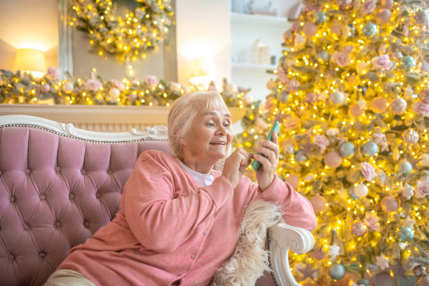 Senior vrouw zittend op een bank en met een smartphone - Foto, afbeelding