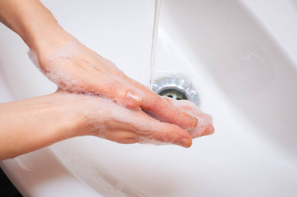 Mujer joven lavándose las manos con jabón sobre el lavabo en el baño. Palmeras juntasvista superior - Foto, Imagen