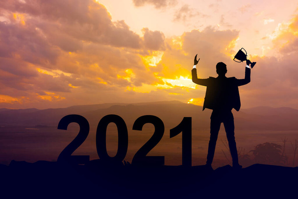 Silhouette businessman holding up a gold trophy cup as a winner in a competition and  2021 years with sunset background,Success new year concept. - Foto, afbeelding