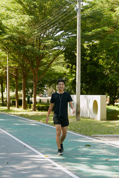 komea nuori aasialainen mies kaveri urheilija Walking kuuntelee musiikkia älypuhelimella yllään urheiluvaatteet, käynnissä ulkona käsite rakastava urheilu terveellistä elämäntapaa polttaa kaloreita - Valokuva, kuva