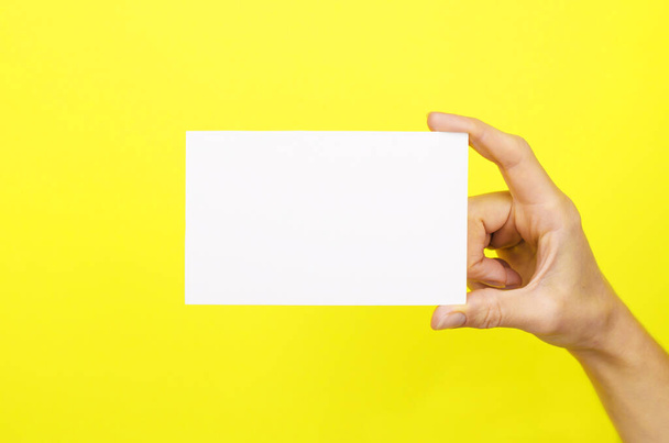 Cartão branco em uma mão feminina sobre um fundo amarelo - Foto, Imagem