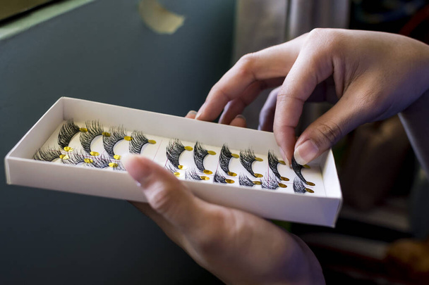 Eine Frau entfernt vorsichtig eine falsche Wimperntusche aus einer Schachtel, die mehrere weitere enthält. Verfahrenseinstellung. - Foto, Bild
