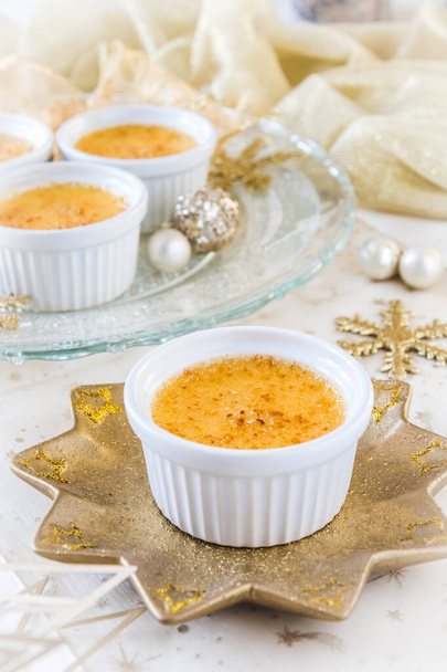 Creme brulee - traditional french vanilla cream dessert with caramelised sugar on top, served on a gold star-shaped plate with gold and white christmas decoration. Vertical stock photo. - Photo, Image