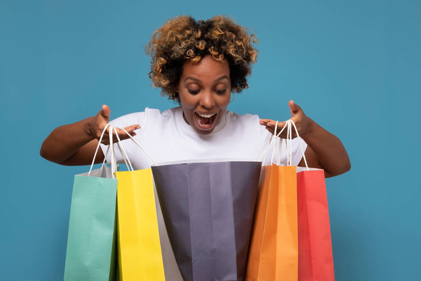 Όμορφη νεαρή Αφρικανή γυναίκα με πολύχρωμες τσάντες για ψώνια που είναι ενθουσιασμένη με τις αγορές της. - Φωτογραφία, εικόνα