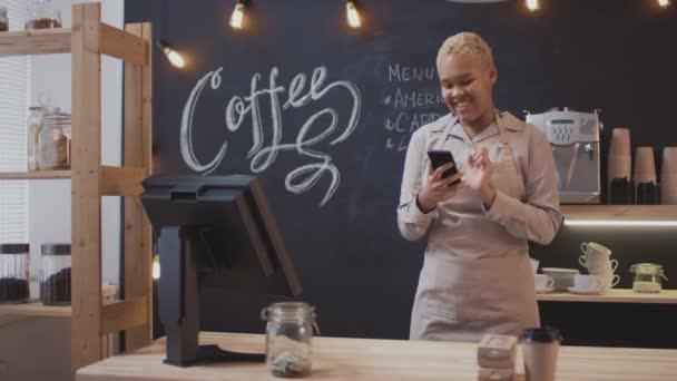 Loop footage of young cheerful woman  smiling and dancing with smartphone working as barista in small local coffee shop enjoying her job - Footage, Video