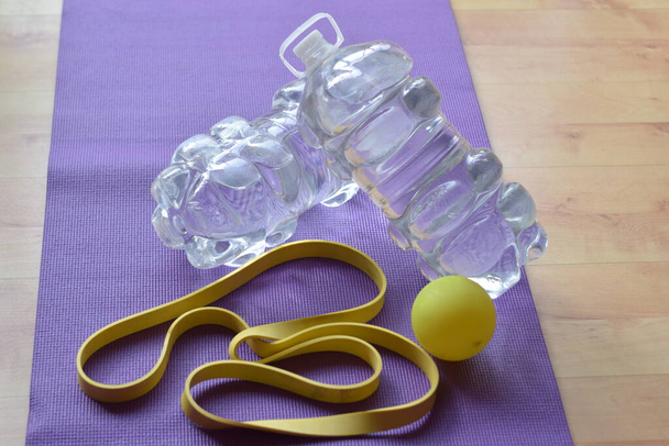Purple mat with water jugs crossed with yellow rubber and yellow rubber - Photo, Image