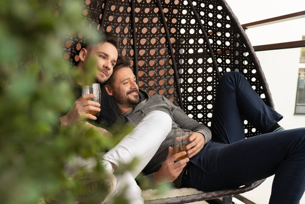 Young boyfriends relaxing and drinking beer on the balcony. Love and affection of same sex partners - Foto, Imagem