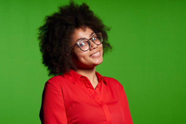 Closeup of smiling young African-American girl in glasses and red shirt looking at camera over green background - Foto, Bild
