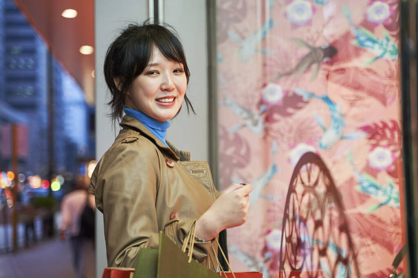 mooie gelukkig jong aziatische vrouw shopper staan in de voorkant van etalage in moderne stad - Foto, afbeelding