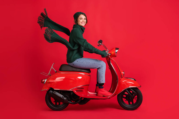Side profile full length portrait of attractive person drive moped x-mas trip jeans boots isolated on red color background - Фото, зображення