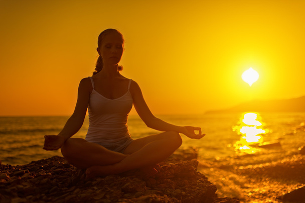Nainen meditoi lootuksessa poseeraa rannalla auringonlaskun aikaan
 - Valokuva, kuva