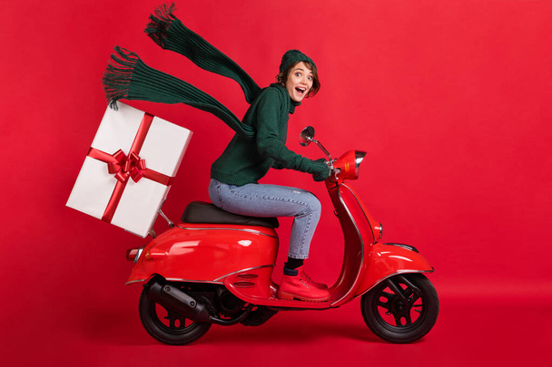 Full size side profile photo of astonished person drive moped x-mas boots jeans gloves isolated on red color background - 写真・画像