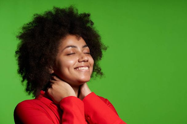 Closeup of pleased African-American girl smiling enjoying with closed eyes, over green background - Photo, Image