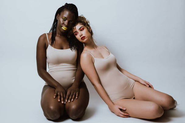 Two girls from different ethnicities posing in studio for a "body positivity" photo session - 写真・画像
