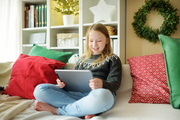 Cute young daughter having online video call on Christmas time. Chatting with distant family during pandemic. Staying safe during winter holidays. Christmas celebration using modern gadgets. - Foto, Bild