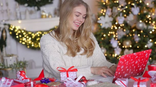 Усміхнена блондинка в затишному зимовому светрі використовує ноутбук для інтернет-магазинів
 - Фото, зображення
