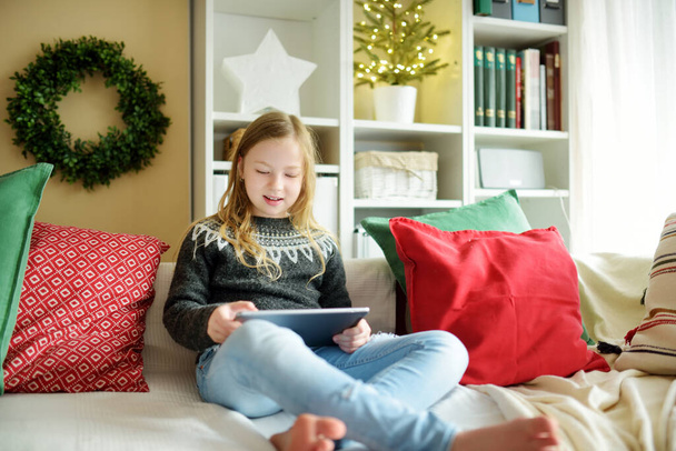 Cute young daughter having online video call on Christmas time. Chatting with distant family during pandemic. Staying safe during winter holidays. Christmas celebration using modern gadgets. - Φωτογραφία, εικόνα