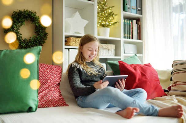 Cute young daughter having online video call on Christmas time. Chatting with distant family during pandemic. Staying safe during winter holidays. Christmas celebration using modern gadgets. - 写真・画像