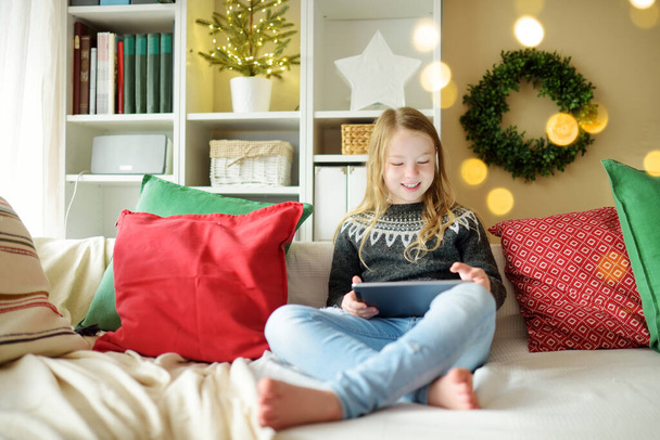 Cute young daughter having online video call on Christmas time. Chatting with distant family during pandemic. Staying safe during winter holidays. Christmas celebration using modern gadgets. - Photo, image