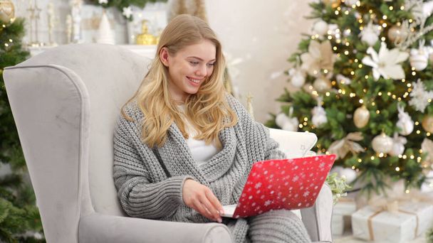 Egy mosolygó nő arcképe, aki laptopot tart az ölében és dolgozik. Kényelmes karosszéken ülve - Fotó, kép
