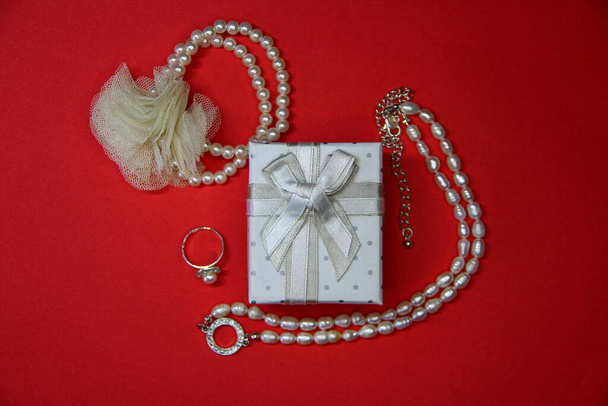 bílá šperkovnice s lukem v blízkosti šperky na červeném pozadí, dárek s kopírovacím prostorem - Fotografie, Obrázek