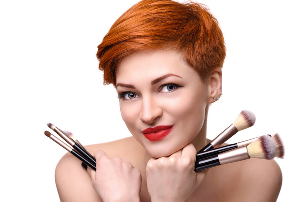 Portrait of a beautiful young woman with short red hair with makeup brushes - Photo, Image