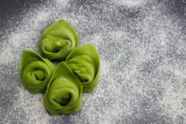 Raw homemade green tortellini on a background of scattered flour. - Foto, afbeelding