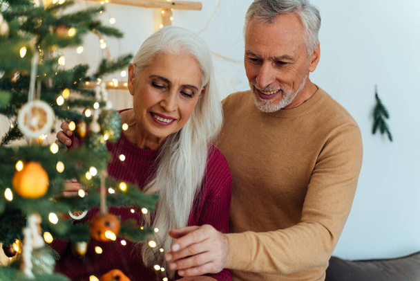 Happy senior couple  making the christmas tree inside their house and preparing for the celebration - Foto, Imagen