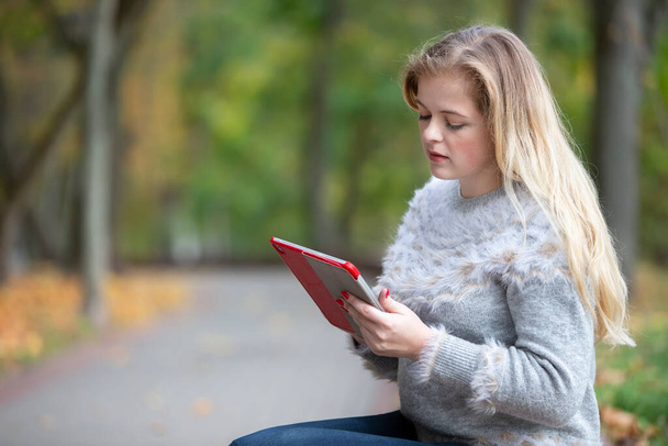 Fiatal gyönyörű nő a parkban egy táblagéppel vagy e-book. - Fotó, kép