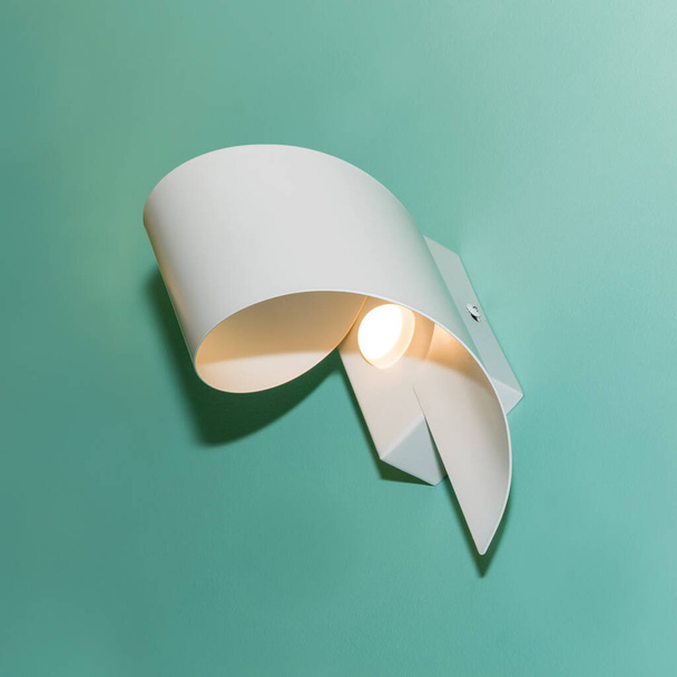 One glowing white modern metal led lamp on the turquoise color wall. Free space. - 写真・画像