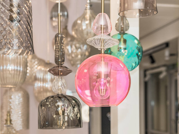 A group of switched-off multicolored lamps with a gray, turquoise, pink glass ceiling is suspended in the white interior. Concept of hotel decoration. Inside. Close up. - Foto, imagen