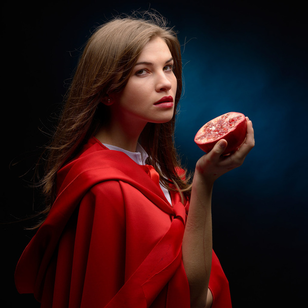 beautiful woman with red cloak holding pomegranate in studio - Foto, Imagen
