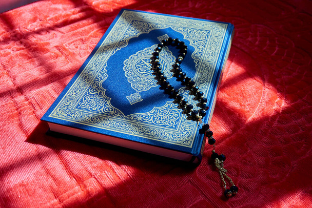 Cuentas de oración en el Corán sobre la alfombra de oración roja con luz solar - Foto, Imagen