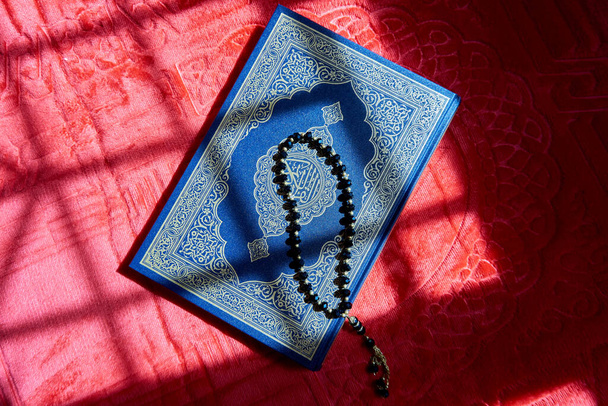 Perles de prière sur le Coran sur le tapis de prière rouge avec la lumière du soleil - Photo, image