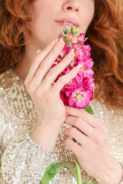 Young woman is holding a pink matthiola flower. Beautiful hands and long natural nails. - Foto, Imagen