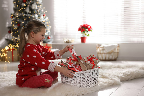 Linda niña tomando regalo del calendario de Adviento de Navidad en casa, espacio para el texto - Foto, imagen