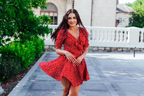 Beautiful brunette woman in red polka dot dress walks the streets of the city - Foto, Bild