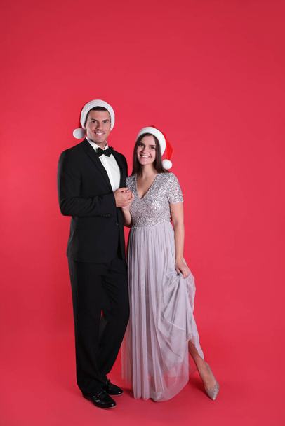 Beautiful happy couple in Christmas hats on red background - Фото, зображення