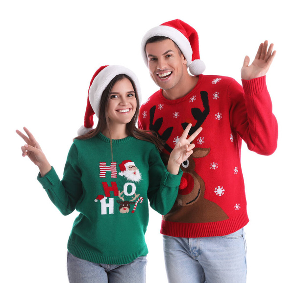 Beautiful happy couple in Santa hats and Christmas sweaters on white background - Фото, изображение
