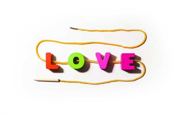 Wooden colorful letters with word Love from colorful letters with holes, strung on a lace in snake shape, with shadows at white background, main word, strong feeling  - Фото, изображение