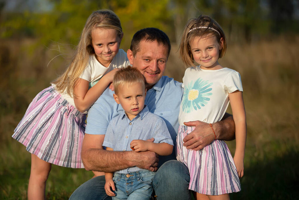 Táta s dcerami a synem se dívají do kamery. Šťastný otec a děti. - Fotografie, Obrázek