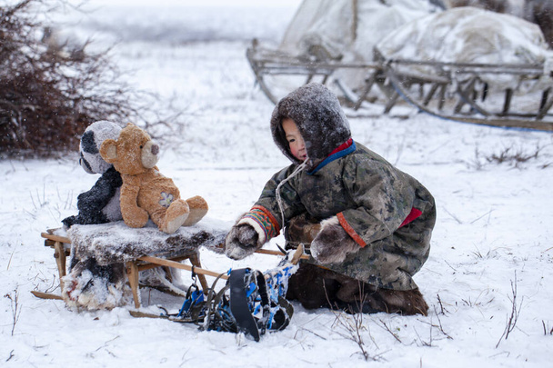 Полуостров Ямал. Олень с молодым оленеводом. Счастливый мальчик на пастбище оленеводов, играющий с игрушками зимой. - Фото, изображение