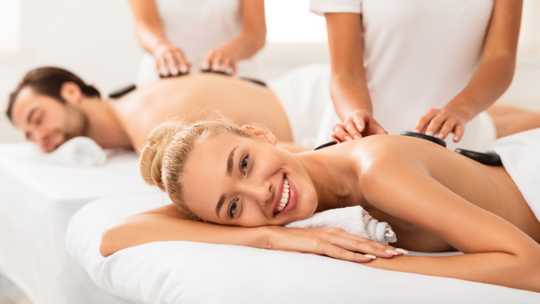 gelukkig vrouw het krijgen van steen massage op koppels spa procedure binnen - Foto, afbeelding