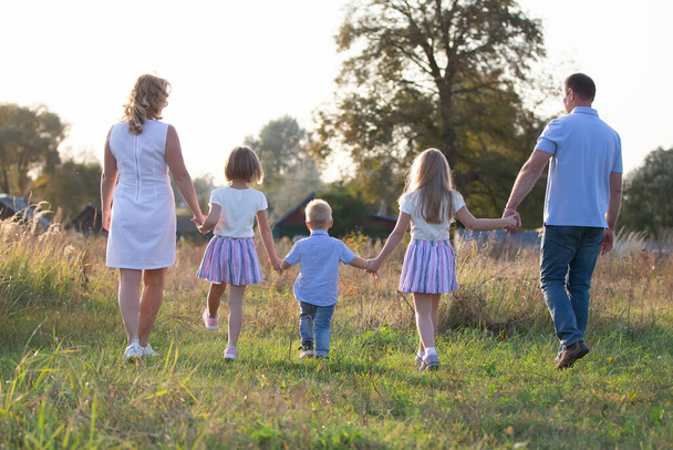 Gelukkige familie: moeder, vader, kinderen, zoon en dochters in de natuur bij zonsondergang. Ouders en kinderen lopen samen. De grote familie. - Foto, afbeelding