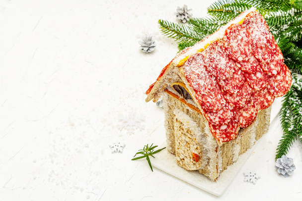 Charcuterie chalet or The Meat Hut as Christmas newest food trend. New Year Keto gingerbread house with traditional decor and symbols. White snow background, copy space - Photo, Image