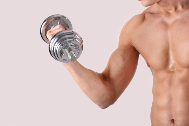 Cropped view of strong millennial sportsman with sexy body lifting dumbbell on light studio background, copy space - Foto, imagen