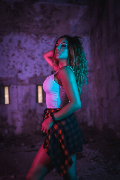 Lifestyle, portrait of a young Caucasian woman in a pose, wearing a tight white shirt and a plaid shirt at the waist. Pink and blue neon lights, urban photography - Foto, Imagem