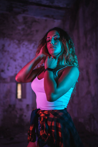 Lifestyle, portrait of a young Caucasian woman in a pose, wearing a tight white shirt and a plaid shirt at the waist. Pink and blue neon lights, urban photography - Fotó, kép