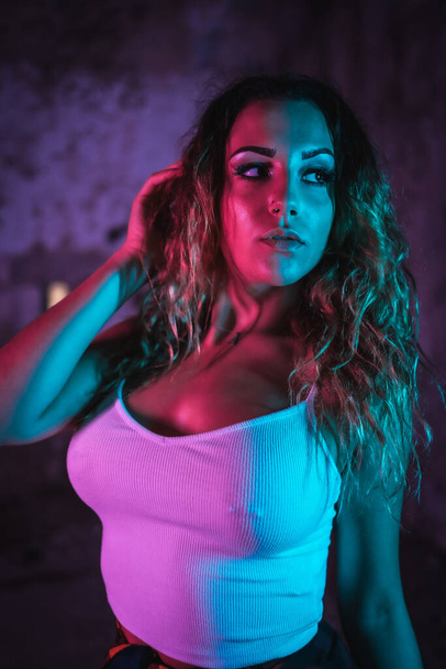 Lifestyle, portrait of a young Caucasian woman in a tight white shirt. Pink and blue neon lights, urban photography of a trap dancer looking sideways - Фото, изображение